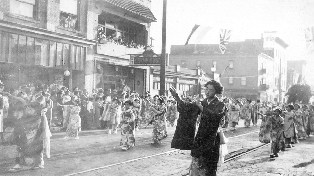 1937: Crowds watch Japanese women and girls in traditional clothes taking part in a parade down Powell Street. (Vancouver Archives)