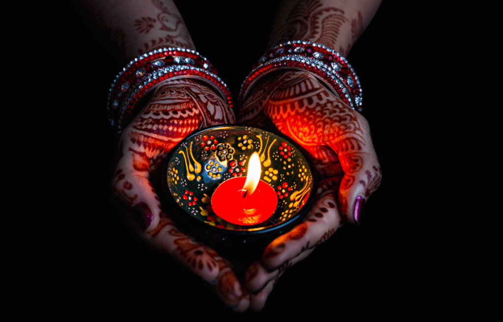 Diwali - Woman hands with henna holding lit candle (Pikoso.kz/Shutterstock)