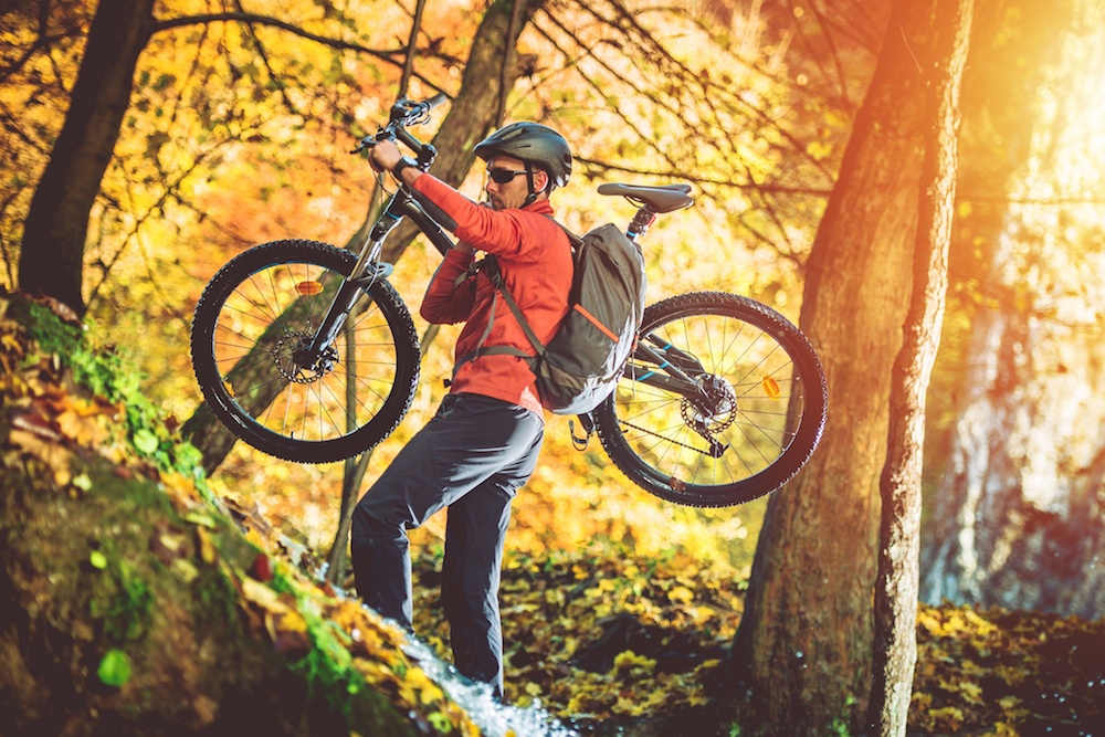 mountain biker carrying his bike up the trail (welcomia/Shutterstock)