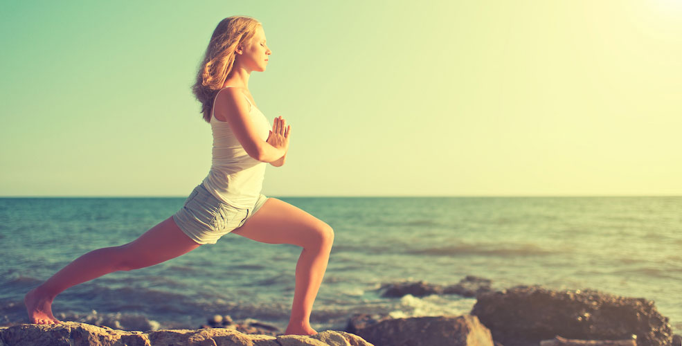 Young woman doing yoga on coast of sea of beach