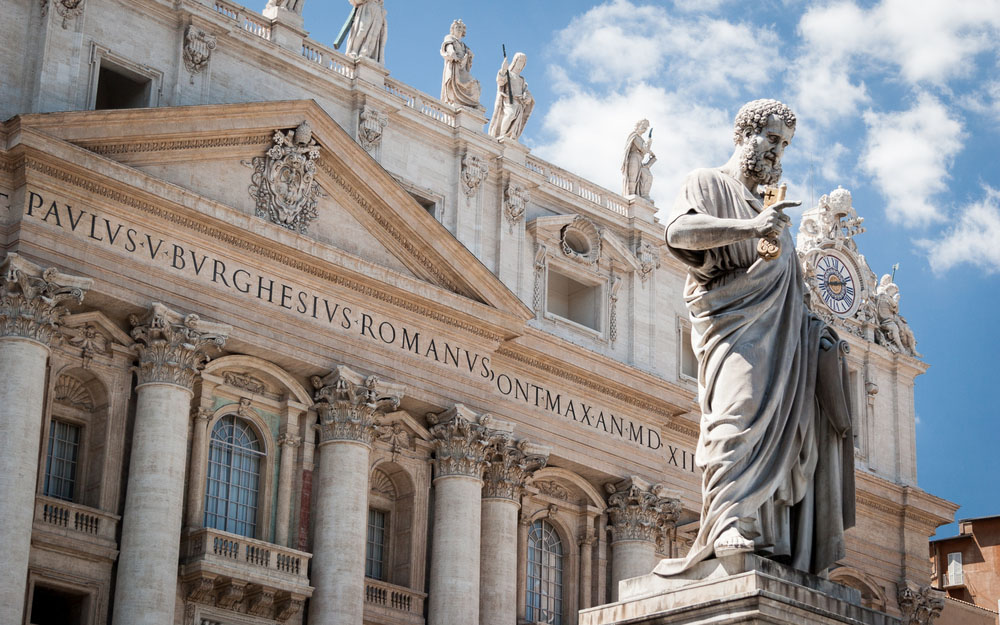 Low angle view of the statue of St. Peter in St. Peter's Square, Vatican City, with the front of the famous Basilica in the background. (pxl.store/Shutterstock)